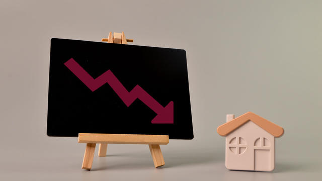 Toy house and arrow down drawn on chalkboard. Falling real estate prices market 