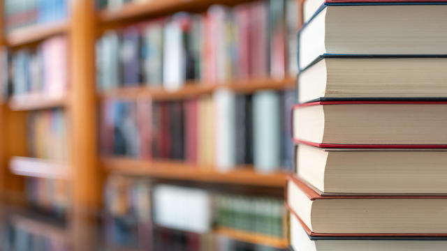 Many books stacked with blurred background of bookstore full of books. Photo with copyspace. 