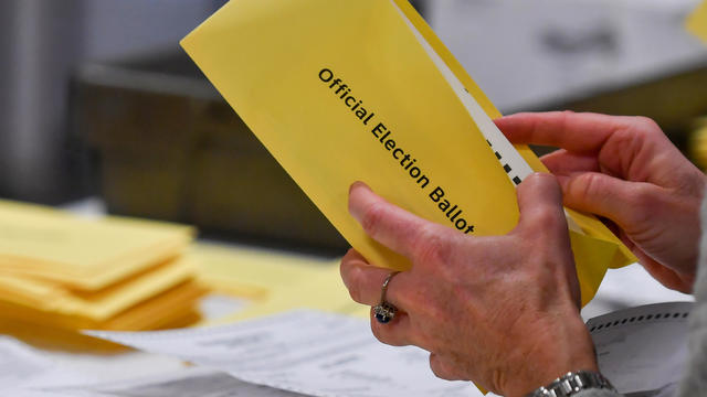 A woman takes a mail-in ballot from an envelope at a polling 