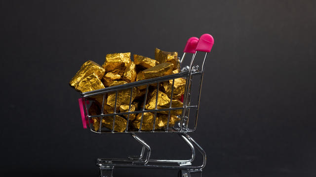 A pile of gold nuggets or gold ore in shopping cart or supermarket trolley on black background, precious stone or lump of golden stone, financial and business concept. 