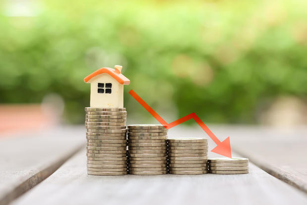 Housing finance and mortgage rates. House model on stack of coins and arrow down, Refinance, Low Interest Loan, Inflation, Deflation, sale price and house tax concept. 