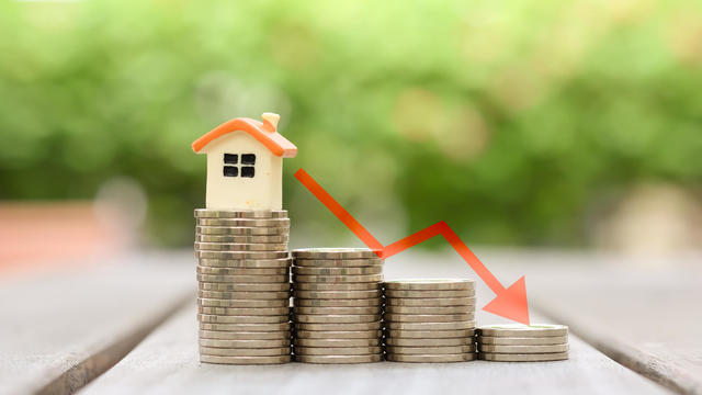 Housing finance and mortgage rates. House model on stack of coins and arrow down, Refinance, Low Interest Loan, Inflation, Deflation, sale price and house tax concept. 