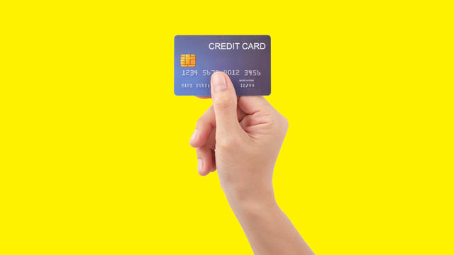 Female hand holding blue credit card on yellow background 