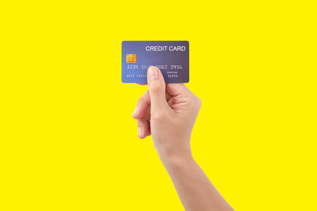 Female hand holding blue credit card on yellow background 