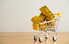 Gold bars in shopping trolley on wooden table with white wall background copy space. 