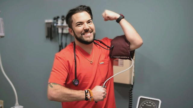 Brandon Downey poses for a photo in an exam room wearing orange scrubs 