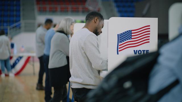 Elderly male voter with bulletin in hands comes to voting booth 