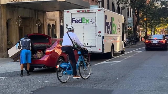 A cyclist rides around a truck and car parked in the bike lane in front of the Drake in Philadelphia 