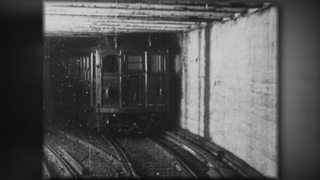 A black-and-white still image of a New York City subway in a tunnel in the early 1900s. 