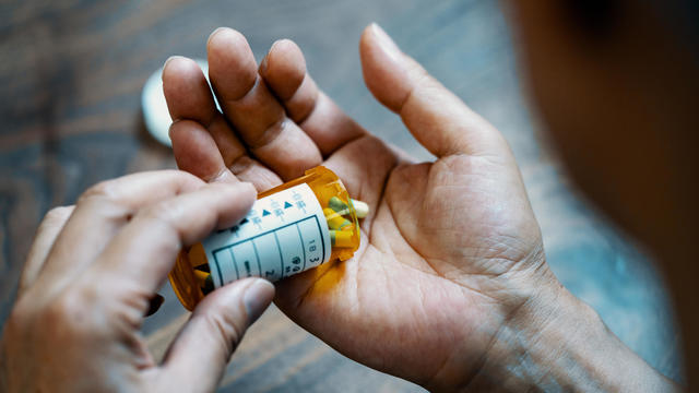 Close-up of a male hand holding a pill bottle pouring medication into his hand 