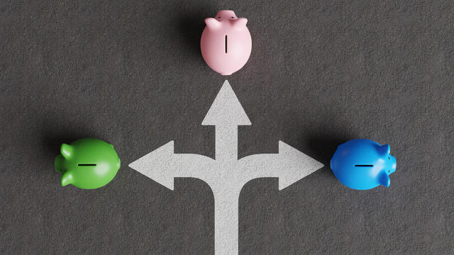 White divided road sign mark on asphalt with 3 different colored piggy banks going to different directions. Illustration of the concept of stock picks and varied investment products 