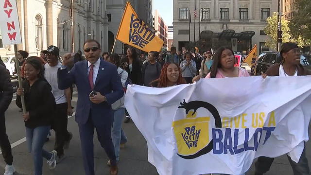 Students and adults walk near City Hall holding sings and banners about voting 