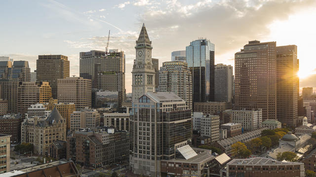 Financial district of Boston, Massachusetts. Skyscrapers skyline with famous Custom House Clock Tower and Faneuil Hall in the evening with visible sunbeam. 