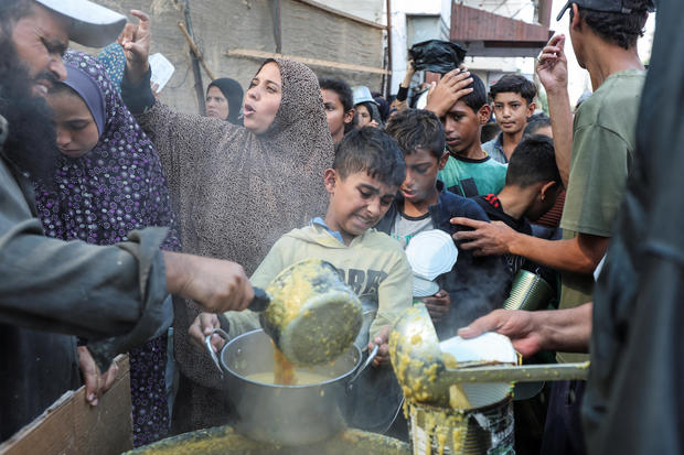 Palestinians gather to receive meals cooked by a charity kitchen, in Deir Al-Balah, central Gaza Strip 