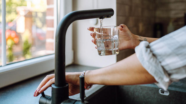 Water filtration in domestic kitchen. Unrecognizable woman hands pouring water in drinking glass from tap 