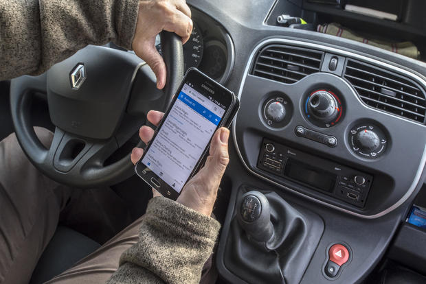 Irresponsible man at steering wheel checking messages on smart phone while driving car on road. 