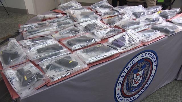 Dozens of guns in bags on display on a New York County District Attorney table. 