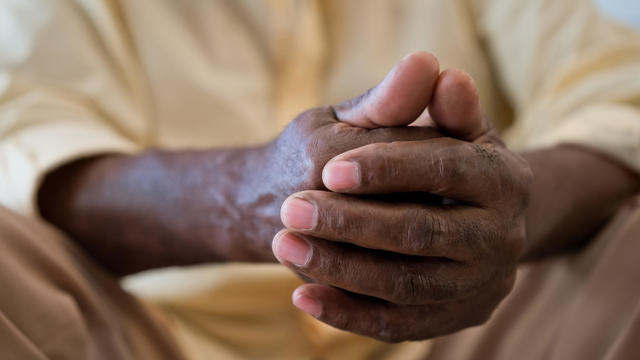 Senior man with hands clasped sitting in living room 