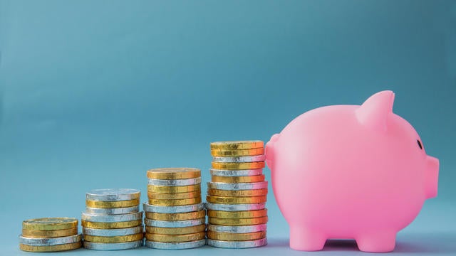 Children savings concept with stacks of gold and silver coins in an upward growth profit graph leading towards a pink, kids Piggy bank 