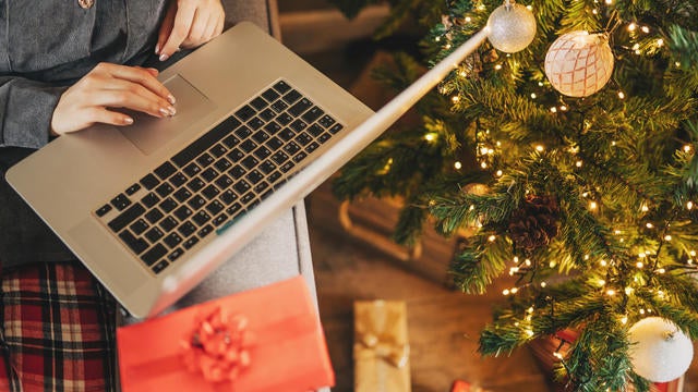 Close up of woman hands with, gifts, coffee cup and laptop. Online shopping at Christmas holidays. Freelance girl woking from home office. Female typing at notebook computer. Christmas moments. 