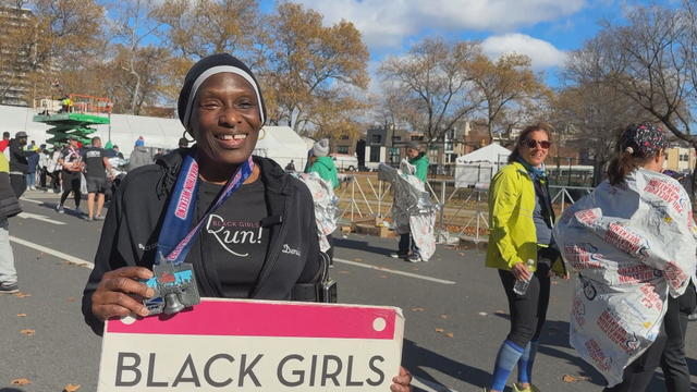 Denise Hall smiles for a photo holding her medal and a Black Girls Run sign near the finish line of the Philadelphia Half Marathon 