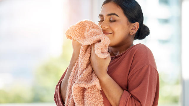 Woman smelling clean laundry, blanket or fabric for fresh and clean smell in house after doing washing, cleaning and housekeeping. Happy female cleaner with textile for aroma, fragrance and scent 