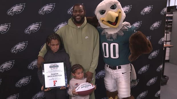 Damon Brockington poses for a photo with Swoop and others in front of an Eagles backdrop 