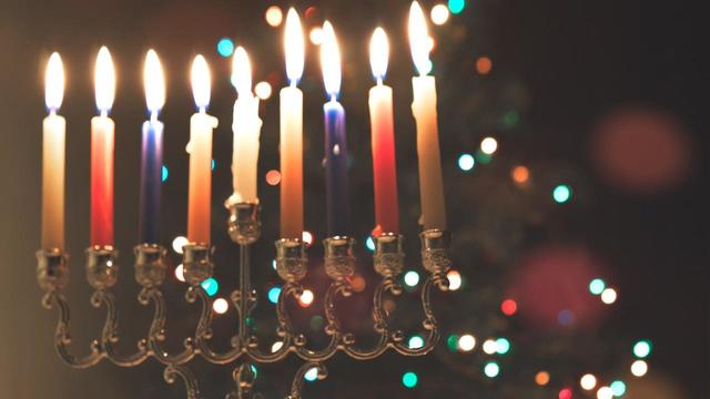 Hanukkah traditional chandelier (menorah) burning candles and spinning top toys (dreidels) on the background of a Christmas tree with colorful lights 