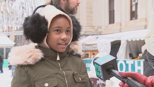 A girl speaks to a reporter near the ice rink at Dilworth Park, she's wearing a green coat and black earmuffs 