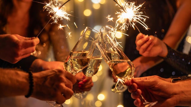 Young friends clinking glasses of champagne in a nightclub. Group of happy people holding sparklers at the party. Celebration, people and holidays concept. 