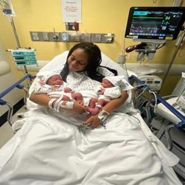 A mom holds newborn twins in her arms in a hospital bed. 