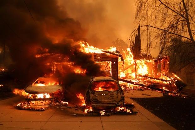 Vehicles and a house burn as powerful winds fueling devastating wildfires in the Los Angeles area force people to evacuate, at the Eaton Fire in Altadena, California, Jan. 8, 2025. 