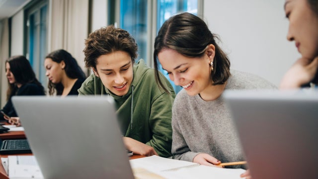 Smiling teenage students studying at desk in school