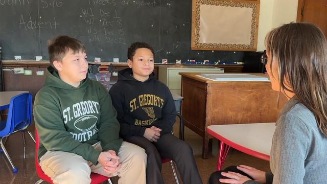 Colin Winn and Christian Fiorillo sit in a classroom and talk to Elle McLogan. 