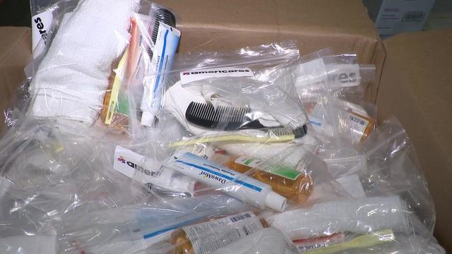 A box full of plastic bags containing toothpaste, small towels, tooth brushes, combs and other hygiene items. 