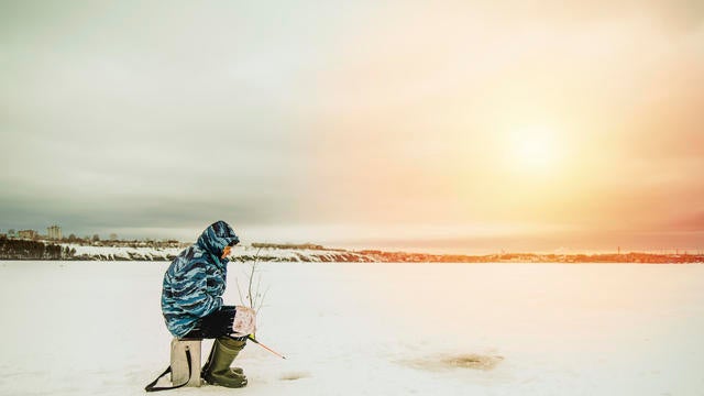 Man ice fishing in frozen lake 