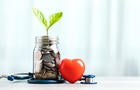 Savings concept for future healthcare. A jar filled with coins and a small plant in the center, accompanied by a heart and a stethoscope, symbolizing saving money for good health in the future 