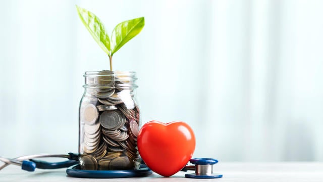 Savings concept for future healthcare. A jar filled with coins and a small plant in the center, accompanied by a heart and a stethoscope, symbolizing saving money for good health in the future 