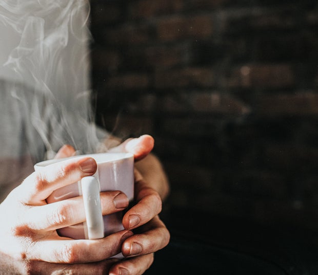 Hands gripping a hot, steaming mug of coffee 