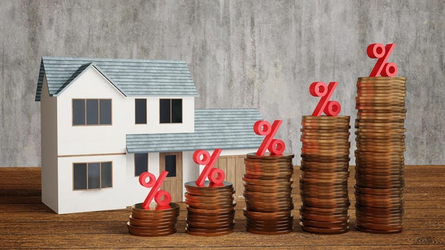 Model house and stacks of gold coins having a red percentage sign on top on a wooden table. Illustration of the concept of increasing interest rate and mortgage loan burden 