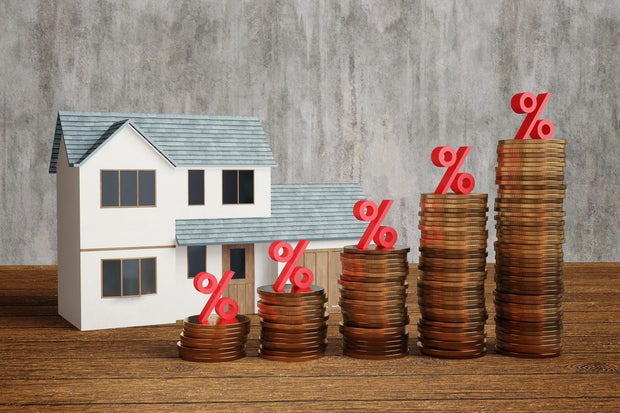 Model house and stacks of gold coins having a red percentage sign on top on a wooden table. Illustration of the concept of increasing interest rate and mortgage loan burden 