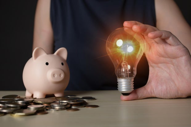 Woman holding light bulb and savings bank and coins with savings, investment, bank and finance concept 
