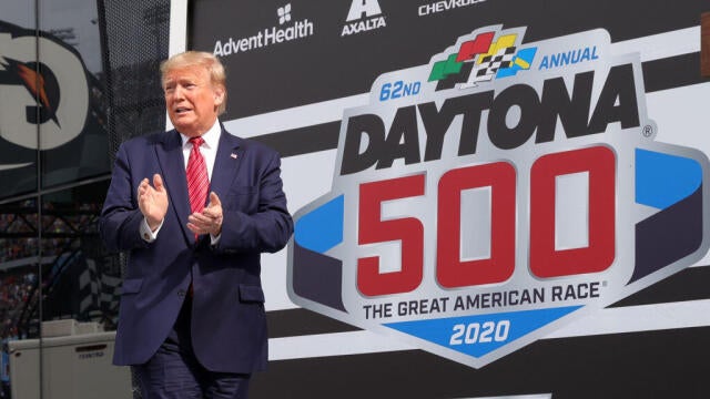 President Donald Trump speaks as first lady Melania Trump looks on from Victory Lane before Daytona 500 in Daytona Beach, Florida, on Feb. 16, 2020. 