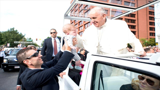 A security guard hands a baby to Pope Francis as he rides on the pope-mobile through Philadelphia 