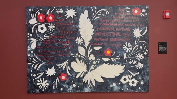 "Cities of the War" painting hangs on a red wall 