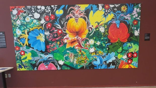 The "Petrykivka Garden" mural hands on a red-painted wall 