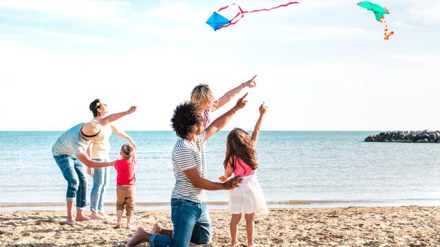 Multiple families composed by parents and children playing with kite at beach vacation - Summer joy life style concept with candid people having fun together at seaside - Bright vivid filter 