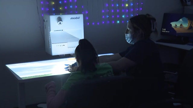 A young woman with special needs sits in a sensory room with a health care professional. 