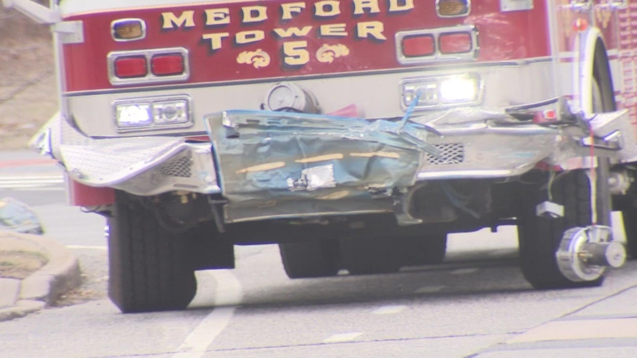 A sedan door stuck on the front bumper of a fire truck. 