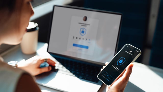 Over the shoulder view of young woman logging in online account with Two-Factor Authentication (2FA) security system visa smart phone and laptop 